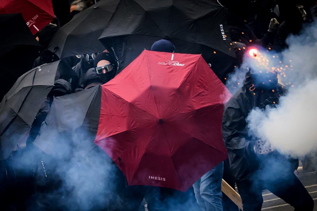 在法国南特市的劳动节集会，抗议者用打开的雨伞保护自己，并向防暴警察投掷烟火。（图取自法新社）